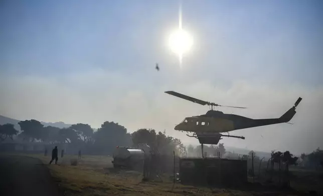 A helicopter refills its water reservoir near Penteli, northeast of Athens, Greece, Monday, Aug. 12, 2024. Hundreds of firefighters backed by dozens of water-dropping planes and helicopters were battling the flames from first light Monday. (AP Photo/Michael Varaklas