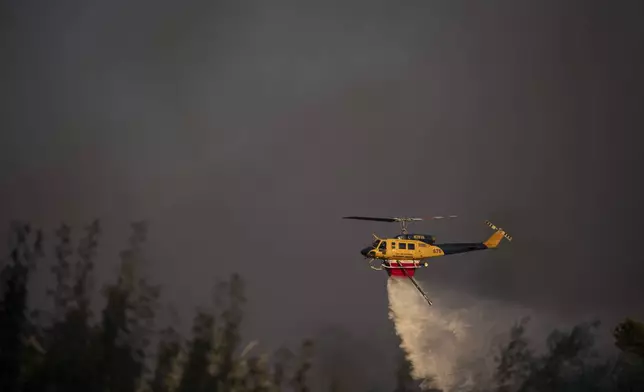 A helicopter drops water near Varnava village during a wildfire, north of Athens, Greece, Sunday, Aug. 11, 2024, with many regions of the country on high alert due to high temperatures and wind speeds. (AP Photo/Michael Varaklas)