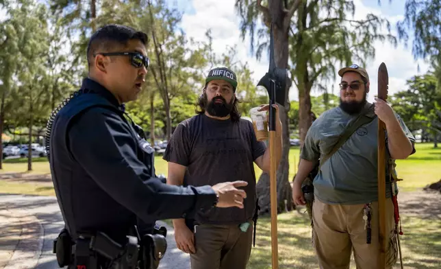 Andrew Roberts, center, director of the Hawaii Firearms Coalition, holds a halberd while talking to a Honolulu police officer at Kapiolani Park on Saturday, June 22, 2024, in Honolulu, Hawaii. (AP Photo/Mengshin Lin)