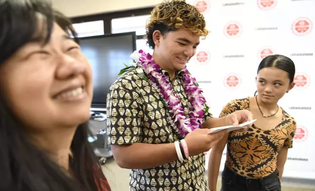 Lahainaluna High School 2024 graduate Talan Toshikiyo, center, stands by little sister Taleah Toshikiyo and school college and career counselor Ginny Yasutake as he opens his scholarship announcement in the school's library Wednesday, July 31, 2024, in Lahaina, Hawaii. (AP Photo/Matthew Thayer)