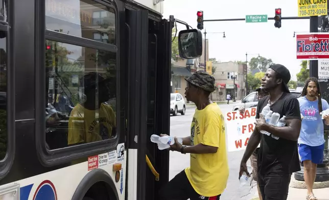 FILE - Volunteers from Saint Sabina Church climb aboard a bus to distribute bottles of cold water at a busy South Side intersection in Chicago, Aug. 27, 2024. (AP Photo/Teresa Crawford, File)