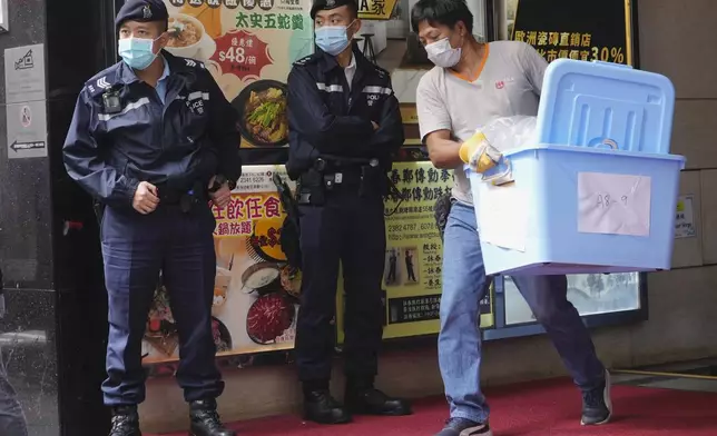 FILE - A worker carrying some containers walks past police officers during a raid on the office of Stand News during a raid in Hong Kong, Dec. 29, 2021. (AP Photo/Vincent Yu, File)