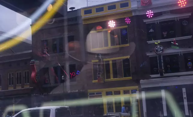 A cowboy hat-wearing musician is reflected on a window as he sings and plays country music at Robert’s Western World as Broadway bars are reflected on a window of the iconic Nashville honky tonk on Sunday, July 28, 2024, in Nashville, Tenn. (AP Photo/Luis Andres Henao)