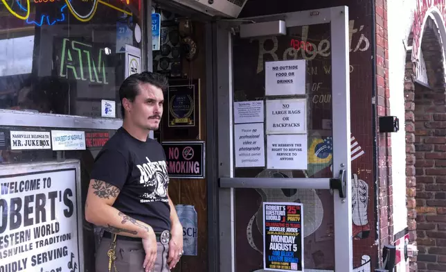 A greeter at Robert’s Western World looks at passersby on Nashville’s Broadway after the Gospel Hour held at the iconic honky tonk on Sunday, July 28, 2024, in Nashville, Tenn. (AP Photo/Luis Andres Henao)