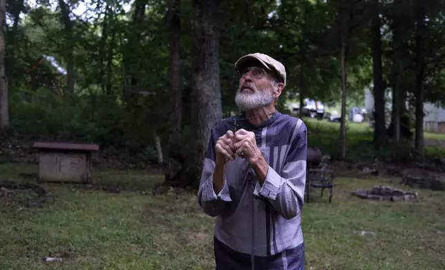 The Rev. Ron Blakely holds a crucifix and prays looking at the trees in the backyard of his log cabin home near Watertown, Tenn., on Friday, July 26, 2024. (AP Photo/Luis Andres Henao)