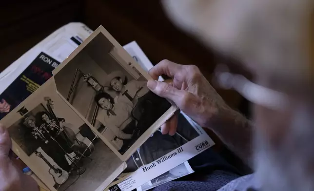 The Rev. Ron Blakely looks at black and white photos of his parents, musicians Jimmy and Dorothy Blakly, at his log cabin home near Watertown, Tenn., on Friday, July 26, 2024. (AP Photo/Luis Andres Henao)