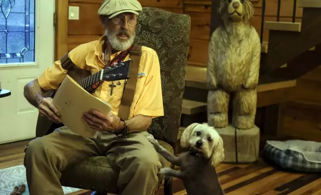 The Rev. Ron Blakely rehearses with sheet music and scripture for his Sunday Gospel Hour at Robert’s Western World honky tonk at his log cabin home near Watertown, Tenn. next to his dog Ope on Friday, July 26, 2024. (AP Photo/Luis Andres Henao)