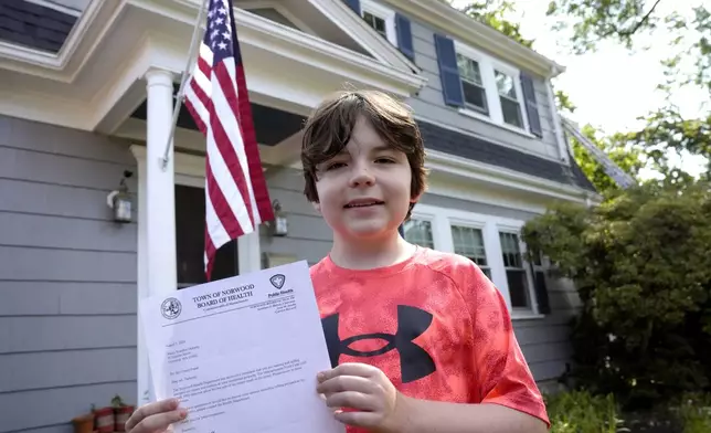 Danny Doherty, 12, of Norwood, Mass., stands for a photograph Wednesday, Aug. 21, 2024, in front of his home in Norwood, while holding a letter from the Town of Norwood Board of Health advising his family that they may not sell homemade ice cream at an ice cream stand near their home. (AP Photo/Steven Senne)