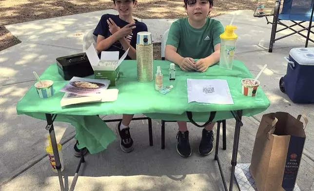 In this Saturday, Aug. 3, 2024 photo provided by Nancy Doherty, Ben Doherty, of Braintree, Mass., left, and his cousin Danny Doherty, 12, of Norwood, Mass., right, sit at a homemade ice cream stand near Danny's home in Norwood. (Nancy Doherty via AP)