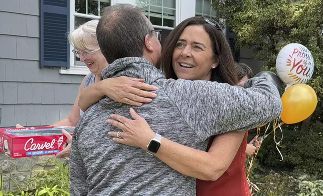 Lori Talanian, right, director of corporate partnerships at Ira Cars, hugs John Quill, center, director and coach of the Boston Bear Cubs hockey team, Wednesday, Aug. 21, 2024, after her company presented the team with a donation of $3,900, at the Doherty family home, in Norwood, Mass. (AP Photo/Michael Casey)