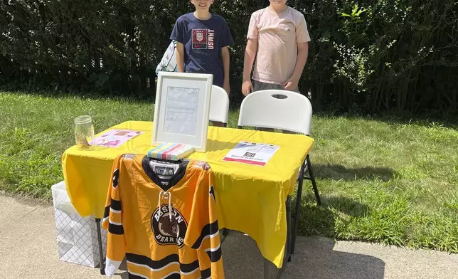 In this Saturday, Aug. 10, 2024 photo provided by Meghan Doherty, Ben Doherty, 12, of Braintree, Mass., left, stands with his cousin Danny Doherty, 12, of Norwood, Mass., right, near a table for donations to the Boston Bear Cubs hockey team, in Norwood. (Meghan Doherty via AP)