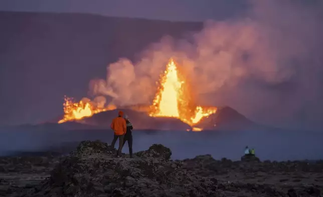 People watch the erupting craters and the lava fountains from the old lava fields around the eruption site on the Reykjanes Peninsula, in Iceland, Wednesday, Aug. 28, 2024. (AP Photo/Marco di Marco)