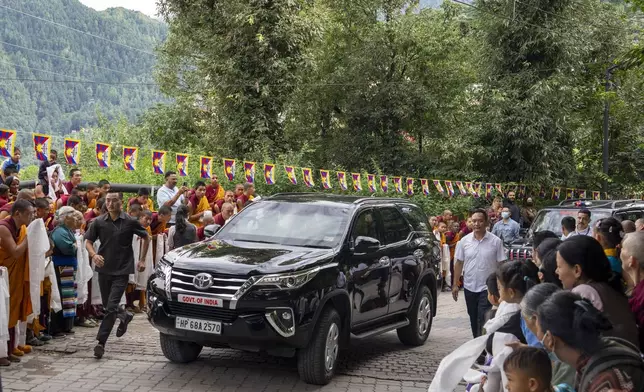 A security person runs along the vehicle in which Tibetan spiritual leader the Dalai Lama sits on his arrival in Dharamshala, India, Wednesday, Aug. 28, 2024. (AP Photo/Ashwini Bhatia)