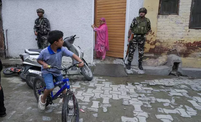 Indian paramilitary soldiers guard as a boy rides on his bicycle during the door-to-door election campaigning by Bharatiya Janata Party (BJP) candidate ahead of the Jammu and Kashmir state assembly elections in Srinagar, Indian controlled Kashmir,Thursday, Aug. 29, 2024. (AP Photo/Mukhtar Khan)