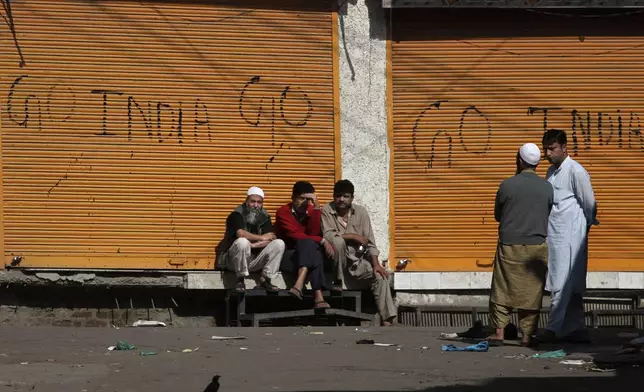 Kashmiris sit outside closed shops painted with graffiti during a curfew in central Srinagar, India, Thursday, Sept. 16, 2010. (AP Photo/Dar Yasin, File)