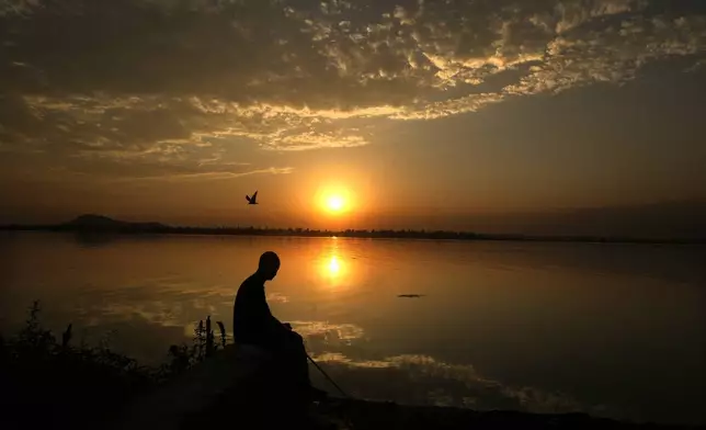 A Kashmiri man fishes as the sun sets over the Dal Lake on a hot summer day on the outskirts of Srinagar, Indian controlled Kashmir, Thursday, July 13, 2023. (AP Photo/Mukhtar Khan, File)