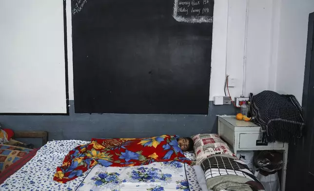 A boy sleeps at a government-run relief camp for survivors set up at a school building third day after landslides set off by torrential rains in Wayanad district, Kerala state, India, Thursday, Aug. 1, 2024. (AP Photo/Rafiq Maqbool)