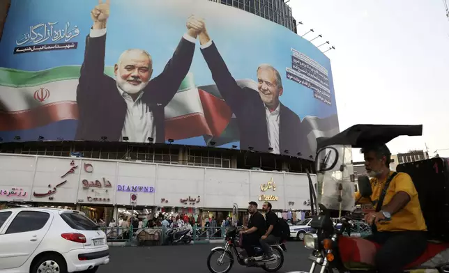 Vehicles drive past a huge banner showing the late Hamas leader Ismail Haniyeh, left, who was killed in an assassination last week, joining hands with Iranian President Masoud Pezeshkian, in a square in downtown Tehran, Iran, Monday, Aug. 5, 2024. Iran has vowed to respond with "power and decisiveness" to the targeted killing of Hamas' top political leader, which it blamed on Israel. (AP Photo/Vahid Salemi)