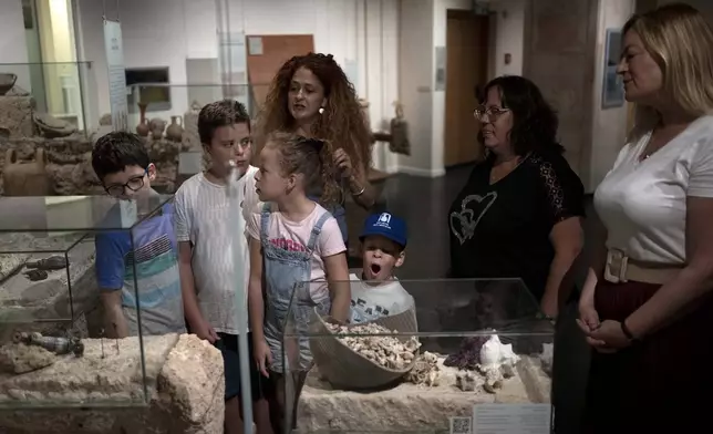 Ariel Heller, 4, center, yawns during the end of a special tour after the child accidentally broke an ancient jar at the Reuben and Edith Hecht Museum in Haifa, Israel, Friday, Aug. 30, 2024. The boy who accidentally broke a rare 3,500-year-old jar in an Israeli museum has been forgiven and invited back, as curators hope to turn the disaster into a teachable moment. (AP Photo/Maya Alleruzzo)