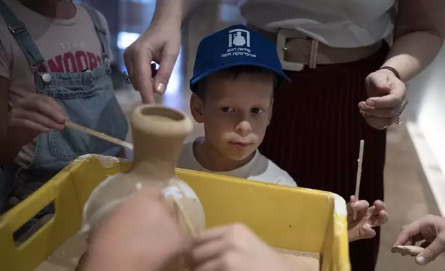 Ariel Heller, 4, helps to glue a broken clay jar during a special tour with his family after he accidentally broke another jar at the Reuben and Edith Hecht Museum in Haifa, Israel, Friday, Aug. 30, 2024. The boy who accidentally broke a rare 3,500-year-old jar in an Israeli museum has been forgiven and invited back, as curators hope to turn the disaster into a teachable moment. (AP Photo/Maya Alleruzzo)