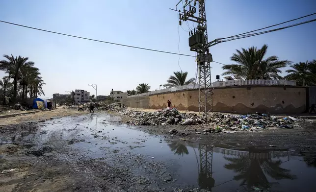 Palestinians displaced by the Israeli air and ground offensive on the Gaza Strip walk next a dark streak of sewage flowing into the streets of Deir al-Balah, central Gaza Strip, Tuesday, Aug. 27, 2024. (AP Photo/Abdel Kareem Hana)