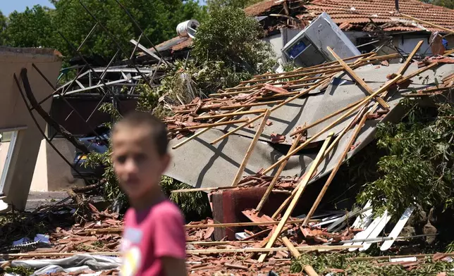 A child stands in the rubble from rocket strikes in Katzrin, in the the Israeli-annexed Golan Heights, Wednesday, Aug. 21, 2024. Lebanon's Hezbollah has launched more than 50 rockets, hitting a number of private homes in the area.(AP Photo/Ariel Schalit)