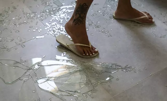 A woman stands on broken glass from the window in her bedroom following an attack from Lebanon, in Acre, north Israel, Sunday, Aug. 25, 2024. (AP Photo/Ariel Schalit)