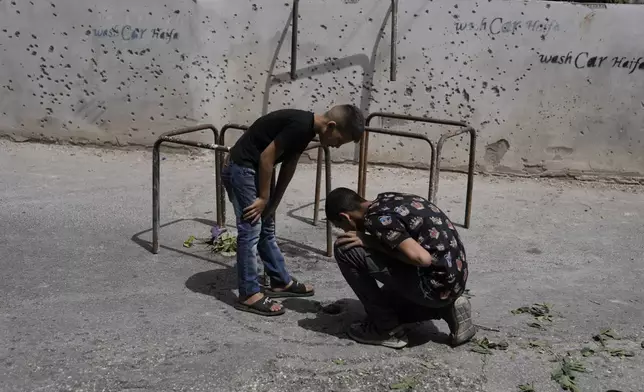 Palestinians check a spot on the ground as they stand next to a wall damaged from shrapnel, following a military operation in the West Bank town of Zababdeh, south of Jenin, Friday, Aug. 30, 2024. (AP Photo/Majdi Mohammed)