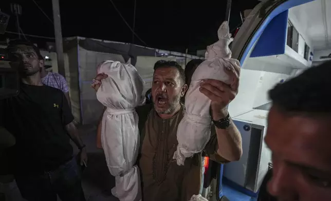 Osama al-Taweel holds up the bodies of his grandchildren who were killed during an Israel airstrike in the Gaza Strip, as he arrives at the hospital morgue in Deir al Balah, Thursday, Aug. 29, 2024. (AP Photo/Abdel Kareem Hana)