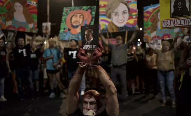 An activist wears theatrical blood, bound wrists and his mouth taped and holds a book depicting Israeli Prime Minister Benjamin Netanyahu as relatives of hostages held by Hamas militants in the Gaza Strip and their supporters call for their immediate release in Tel Aviv, Israel, Saturday, Aug. 24, 2024. (AP Photo/Maya Alleruzzo)