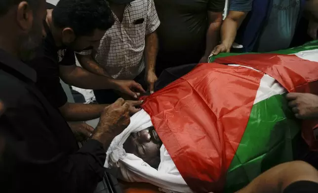 Mourners take a last look at Khalil Ziada, wrapped with a Palestinian flag, who died during an Israeli settler attack in the Wadi Rahal village, at a hospital morgue in the West Bank city of Bethlehem, Tuesday, Aug. 27, 2024. (AP Photo/Mahmoud Illean)