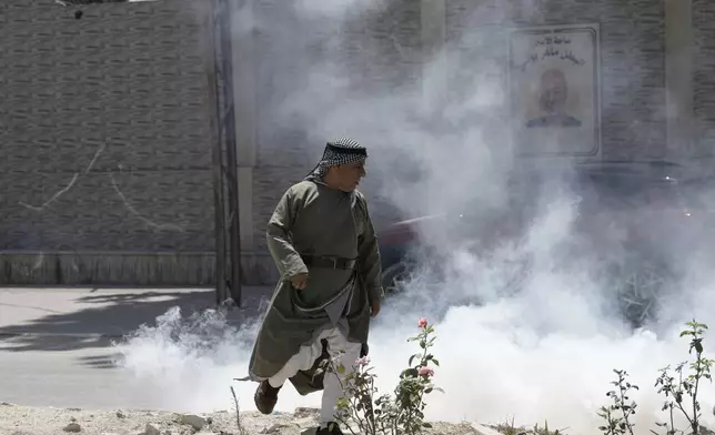 A Palestinian man reacts to tear gas deployed by the Israeli military in Tulkarem refugee camp in the West Bank, Saturday, Aug. 3, 2024. The Israeli military said it struck five suspected terrorists in a vehicle on their way to carry out an attack. (AP Photo/Majdi Mohammed)