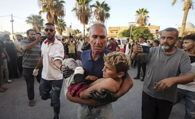 A Palestinian man carries an injured child after an Israeli airstrike in Deir al Balah, Gaza Strip, Tuesday, Aug. 6, 2024. (AP Photo/Abdel Kareem Hana)