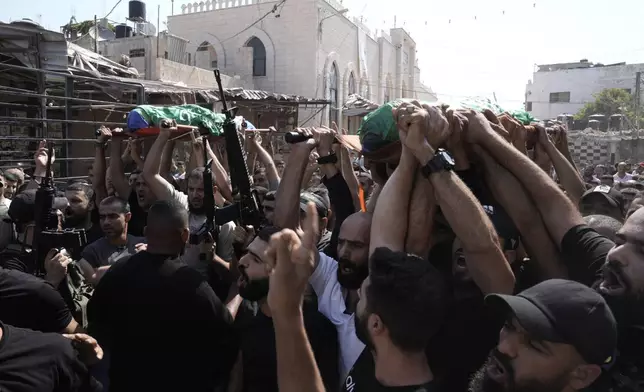 Gunmen march during a funeral with the bodies of Palestinians Ahmed Abu Arra from the town of Aqaba, left, and Raafat Dawasa from the town of Silat Al-Harithiya, both draped in the Hamas flag and killed in an Israeli strike in the Jenin refugee camp, in the West Bank city of Jenin, Sunday, Aug. 18, 2024. Israel's military said Saturday it struck a "terrorist cell" in Jenin. The Palestinian health ministry there said two bodies were taken to a government hospital; Hamas claimed the two men as commanders in its military wing. (AP Photo/Majdi Mohammed)