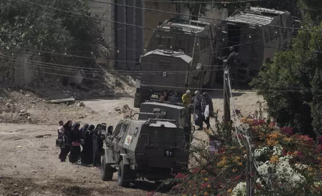 Palestinians stand in line next to Israeli armoured vehicles during a military operation in the West Bank Jenin refugee camp, Saturday, Aug. 31, 2024. (AP Photo/Majdi Mohammed)