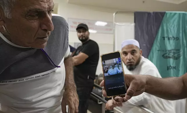 Friends and relatives show a phone with an image of Qaid Farhan Alkadi, 52, who was held hostage by Hamas militants in the Gaza Strip, as they stand at the Soroka Medical Center in Beersheba, Israel, Tuesday, Aug. 27, 2024. (AP Photo/Tsafrir Abayov)