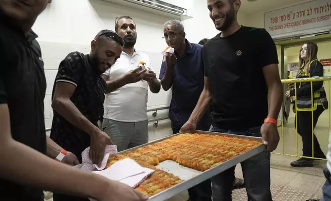 Friends and relatives of Qaid Farhan Alkadi, 52, who was held hostage by Hamas militants in the Gaza Strip, eat a traditional sweet known as knafeh, on a corridor of the Soroka Medical Center in Beersheba, Israel, Tuesday, Aug. 27, 2024. (AP Photo/Tsafrir Abayov)