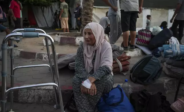 A woman sits on the curb next to her belongings outside the Al-Aqsa Martyrs Hospital in Deir al Balah, Gaza Strip, Sunday, Aug. 25, 2024. (AP Photo/Abdel Kareem Hana)