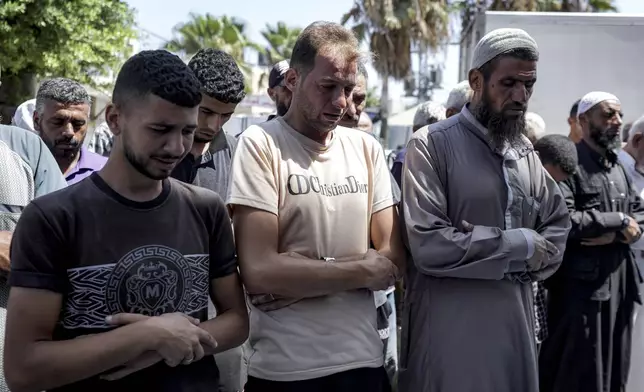 Mohammad Abu Al-Qumsan, Center, prays next to the bodies of his 4-day-old twin children, killed in the Israeli bombardment of the Gaza Strip, at a hospital in Deir al-Balah, Tuesday, Aug. 13, 2024. (AP Photo/Abdel Kareem Hana)