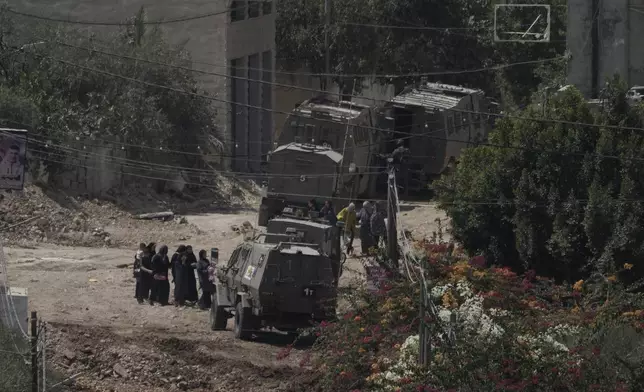 Palestinians stand in line next to Israeli armoured vehicles during a military operation in the West Bank Jenin refugee camp, Saturday, Aug. 31, 2024. (AP Photo/Majdi Mohammed)