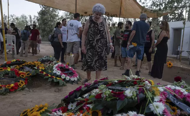 Widow Ruti Munder stands near the grave of her husband Avraham Munder, who was killed in Hamas captivity in the Gaza Strip and recovered by the Israeli military in Gaza, at Kibbutz Nir Oz, southern Israel, Wednesday, Aug. 21, 2024. Their son, Roee Munder, who was killed on Oct. 7, 2023, was reburied at the Kibbutz. (AP Photo/Ohad Zwigenberg)