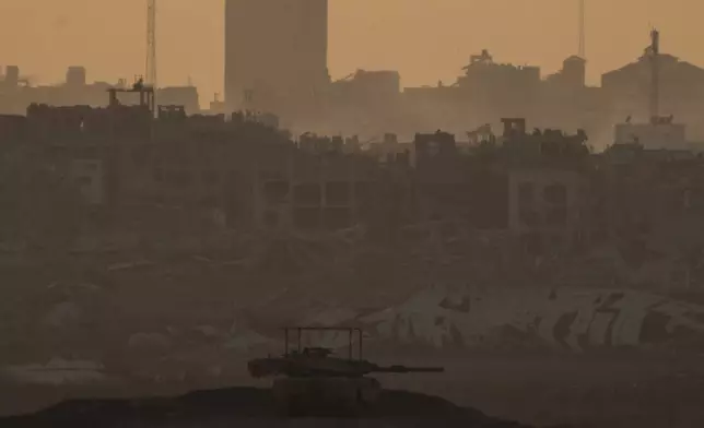 An Israeli tank is seen near the Israeli-Gaza border, with destroyed buildings in the back in the Gaza Strip, as seen from southern Israel, Wednesday, Aug. 21, 2024. (AP Photo/Leo Correa)