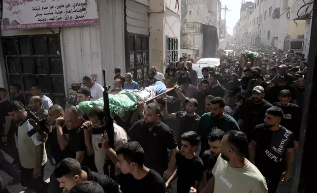 Gunmen march during a funeral with the bodies of Palestinians Ahmed Abu Arra from the town of Aqaba, left, and Raafat Dawasa from the town of Silat Al-Harithiya, both draped in the Hamas flag and killed in an Israeli strike in the Jenin refugee camp, in the West Bank city of Jenin, Sunday, Aug. 18, 2024. Israel's military said Saturday it struck a "terrorist cell" in Jenin. The Palestinian health ministry there said two bodies were taken to a government hospital; Hamas claimed the two men as commanders in its military wing. (AP Photo/Majdi Mohammed)