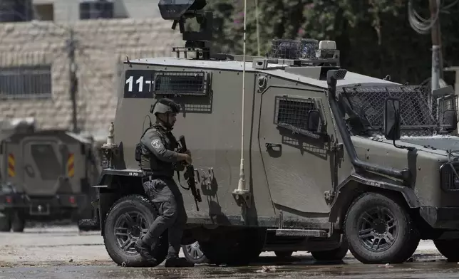 A member of the Israeli forces walks next to an armoured vehicle during a military operation in the West Bank city of Jenin, Wednesday, Aug. 28, 2024. (AP Photo/Majdi Mohammed)