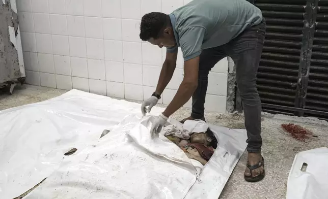 EDS NOTE: GRAPHIC CONTENT - A worker unzips a body bag to display a Palestinian family, consisting of five children aged 2 to 11 and their parents, in the morgue at Al-Aqsa Martyrs Hospital in Deir al-Balah, Gaza Strip, after an Israeli strike hit their home in the Nuseirat refugee camp, Wednesday, Aug. 14, 2024. (AP Photo/Abdel Kareem Hana)