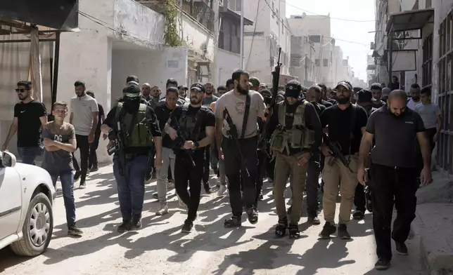 Gunmen march during a funeral for Palestinians Ahmed Abu Arra from the town of Aqaba and Raafat Dawasa from the town of Silat Al-Harithiya, both draped in the Hamas flag and killed in an Israeli strike in the Jenin refugee camp, in the West Bank city of Jenin, Sunday, Aug. 18, 2024. Israel's military said Saturday it struck a "terrorist cell" in Jenin. The Palestinian health ministry there said two bodies were taken to a government hospital; Hamas claimed the two men as commanders in its military wing. (AP Photo/Majdi Mohammed)