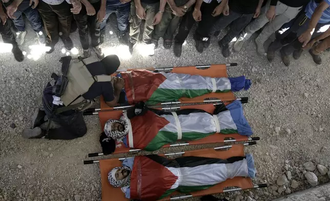 A Palestinian gunman kneels over a Palestinian killed by Israeli fire, at a funeral in the West Bank village of Aqaaba, Tuesday, Aug. 6, 2024. (AP Photo/Majdi Mohammed)