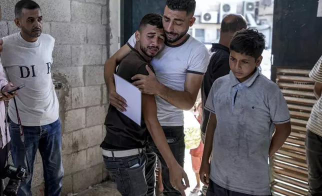 Palestinians mourn their 4-day-old twin relatives, killed in the Israeli bombardment of the Gaza Strip, as he holds their birth certificates, at a hospital morgue in Deir al-Balah, Tuesday, Aug. 13, 2024. (AP Photo/Abdel Kareem Hana)