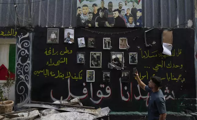 A man takes a picture of a wall displaying photos of Palestinians, who died during previous clashes, following an Israeli military operation in the West Bank refugee camp of Al-Faraa, Thursday, Aug. 29, 2024. (AP Photo/Nasser Nasser)