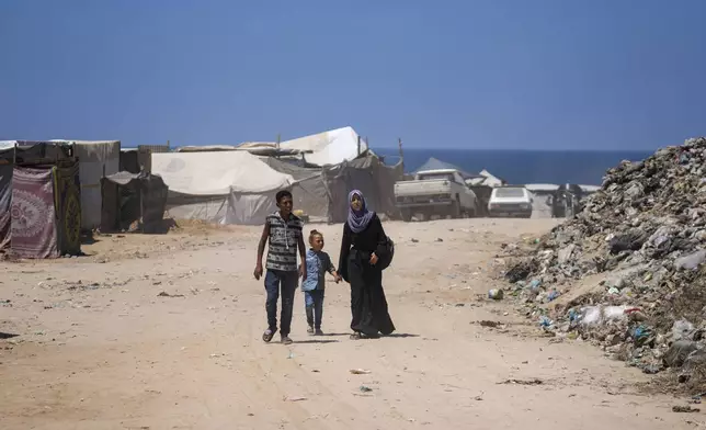 Displaced Palestinians walk past tents pitched on the beach, west of Deir al-Balah, Gaza Strip, Tuesday, Aug. 20, 2024. (AP Photo/Abdel Kareem Hana)